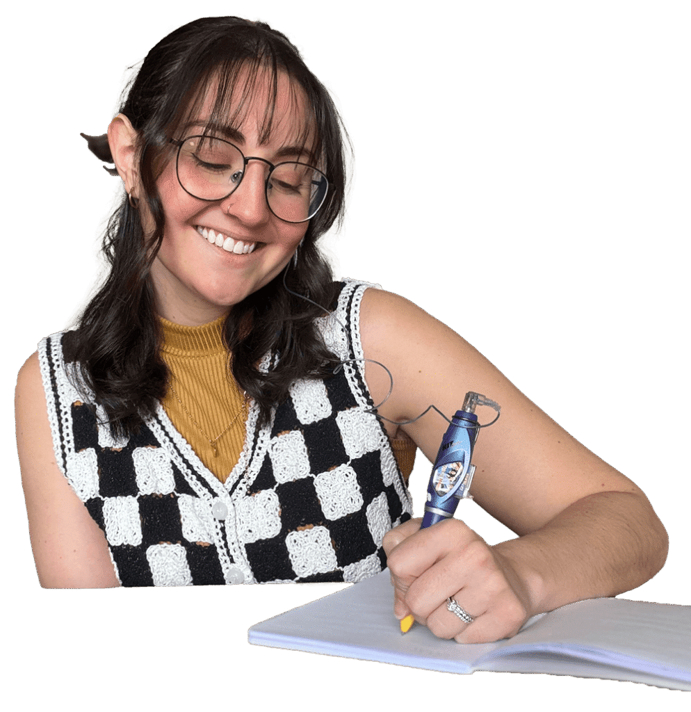A smiling person with glasses and a black and white checkered vest writes with a pen on a notepad. The background is plain black.